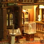 Close-up of the Philosophical Classics Library book nook, featuring stained-glass windows, classical busts, wooden columns and a miniature artifact displayed inside a clear exhibition case.