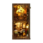 Illuminated front view of the World in a Frame book nook, featuring a two-level miniature art studio with easels, paintings, brushes, shelves, flowers and warm lighting.