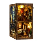 Illuminated front-angle view of the World in a Frame book nook, featuring a two-level miniature art studio, easels, paintings, brushes, shelves, flowers and warm interior lighting.