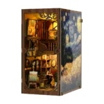 Illuminated left-angle view of the World in a Frame book nook, featuring a two-level miniature art studio, easels, paintings, brushes, shelves and a starry night side panel.