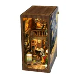 Illuminated right-angle view of the World in a Frame book nook, featuring a two-level miniature art studio with easels, paintings, brushes, shelves, flowers and detailed wooden decor.