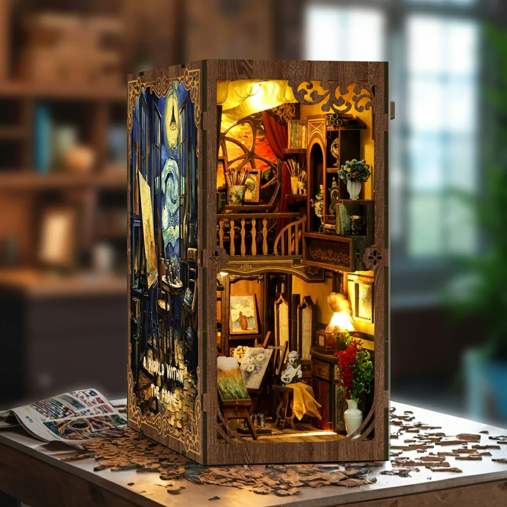 Illuminated angled view of the World in a Frame book nook displayed on a table, featuring a two-level art studio, easels, paintings, shelves, flowers and warm interior lighting.