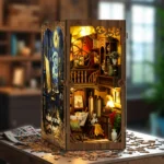 Illuminated angled view of the World in a Frame book nook displayed on a table, featuring a two-level art studio, easels, paintings, shelves, flowers and warm interior lighting.