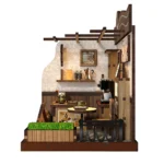 Side view of the completed Country Cafe DIY miniature featuring a coffee table, espresso machine, wall shelf, menu artwork, wooden planter, railing, and café interior details.