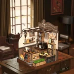 Completed Country Cafe DIY miniature displayed on a wooden desk in a vintage room, featuring a coffee counter, espresso machine, shelves, dining table, menu board, and decorative cat.