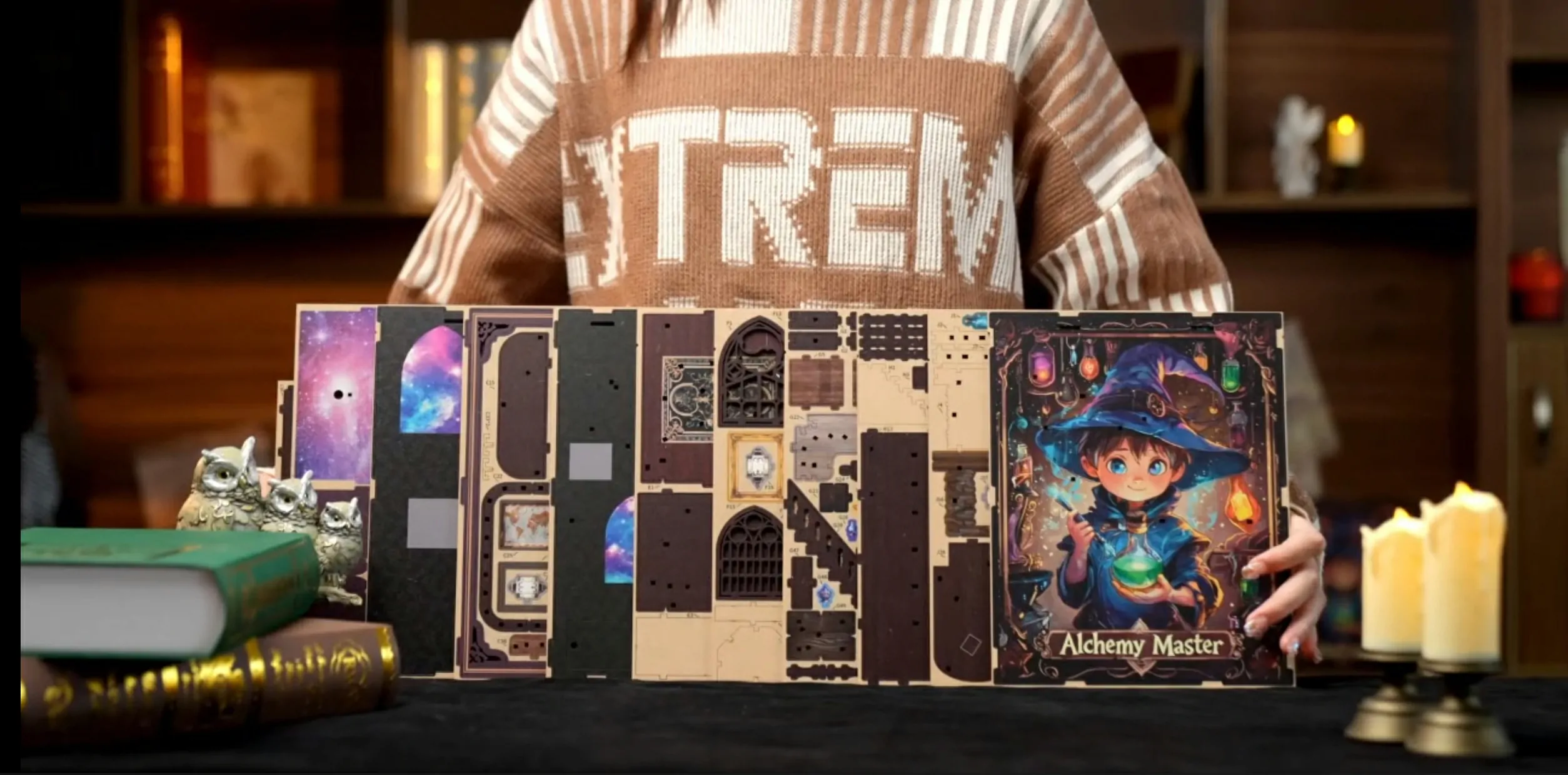 Alchemy Master DIY book nook kit unboxing with precut wooden panels, printed decorative pieces, packaging, and miniature assembly components displayed on a table.