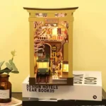 Illuminated front view of the "Japan Street Cat" DIY book nook, featuring a miniature train, a railway crossing, cherry blossom trees, and Japanese architecture.