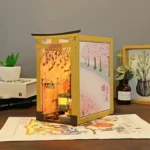Illuminated side view of the Japan Street Cat DIY book nook featuring a miniature train scene and a decorative cherry blossom panel.