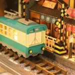 Detail of the "Japan Street Cat" DIY book nook, featuring a miniature train, railway tracks, a level crossing signal, and illuminated Japanese shops.