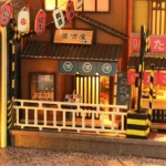 Illuminated detail of the "Japan Street Cat" DIY book nook, featuring a Japanese izakaya, lanterns, a shop window, a railway crossing, and a miniature street.