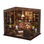 Front view of the Left Bank Reading Room book nook, featuring illuminated bookshelves, a glowing fireplace, leather chairs, framed artwork, plants and detailed wooden furniture.