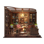 Front view of the completed and illuminated Left Bank Study DIY miniature featuring a glowing fireplace, tall bookshelves, leather chairs, framed artwork, plants, a tea table, and a decorative storage cabinet.