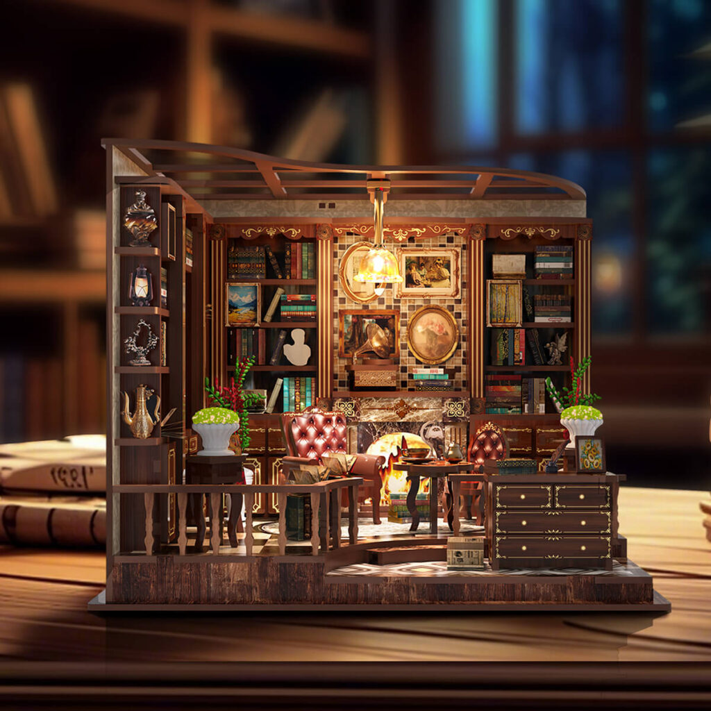 Illuminated front view of the completed Left Bank Study DIY miniature featuring a glowing fireplace, tall bookshelves, leather chairs, framed artwork, plants, a tea table, and a hanging lamp.