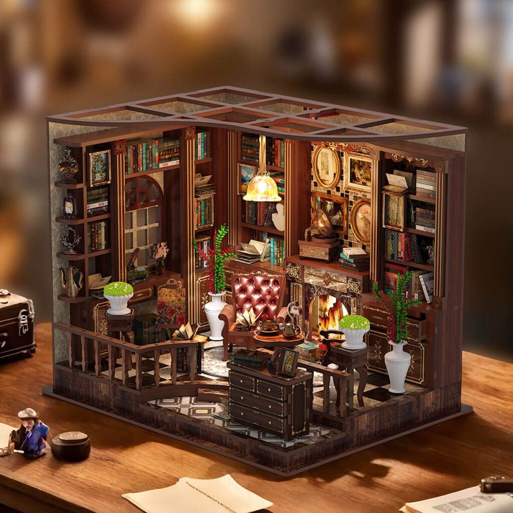 Completed and illuminated Left Bank Study DIY miniature displayed on a wooden desk, featuring tall bookshelves, leather chairs, a glowing fireplace, framed artwork, plants, and a hanging lamp.