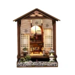 Illuminated front view of the Zen Mooslaterne DIY kit, featuring a Japanese house, Zen garden, bonsai, stone lantern, and miniature tea room.