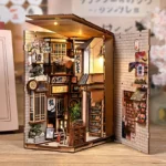 An open, well-lit view of the "Japanese Alley with Cat" DIY kit, featuring a Japanese alleyway, miniature shops, lanterns, parasols, plants, and shelving units.